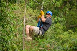 man zooming across a rainforest field on blue river zipline
